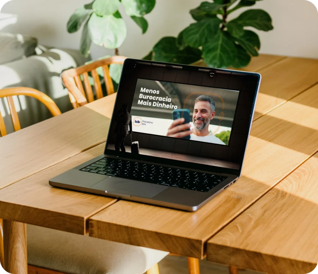 Laptop aberto com ecrã a mostrar "Menos Burocracia Mais Dinheiro" e homem sorridente